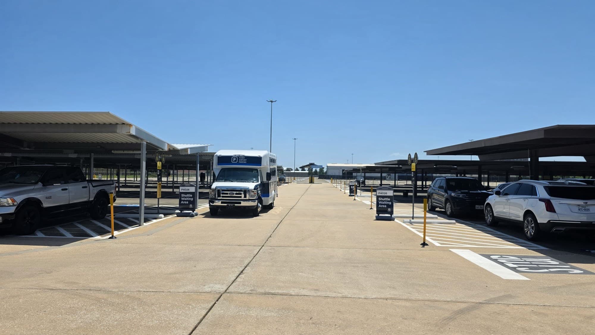 The Hobby Airport Parking lot near Houston Hobby Airport: the free 24/7 shuttle waiting between rows of covered steel-canopy parking under a clear sky